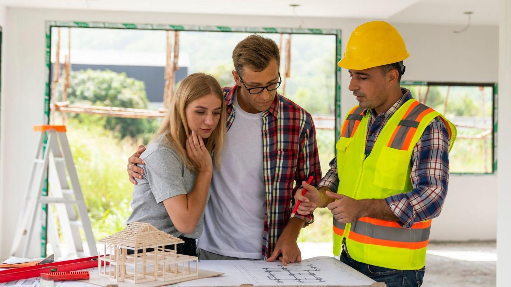 A couple looks at plans with a builder in their home, which is under renovation