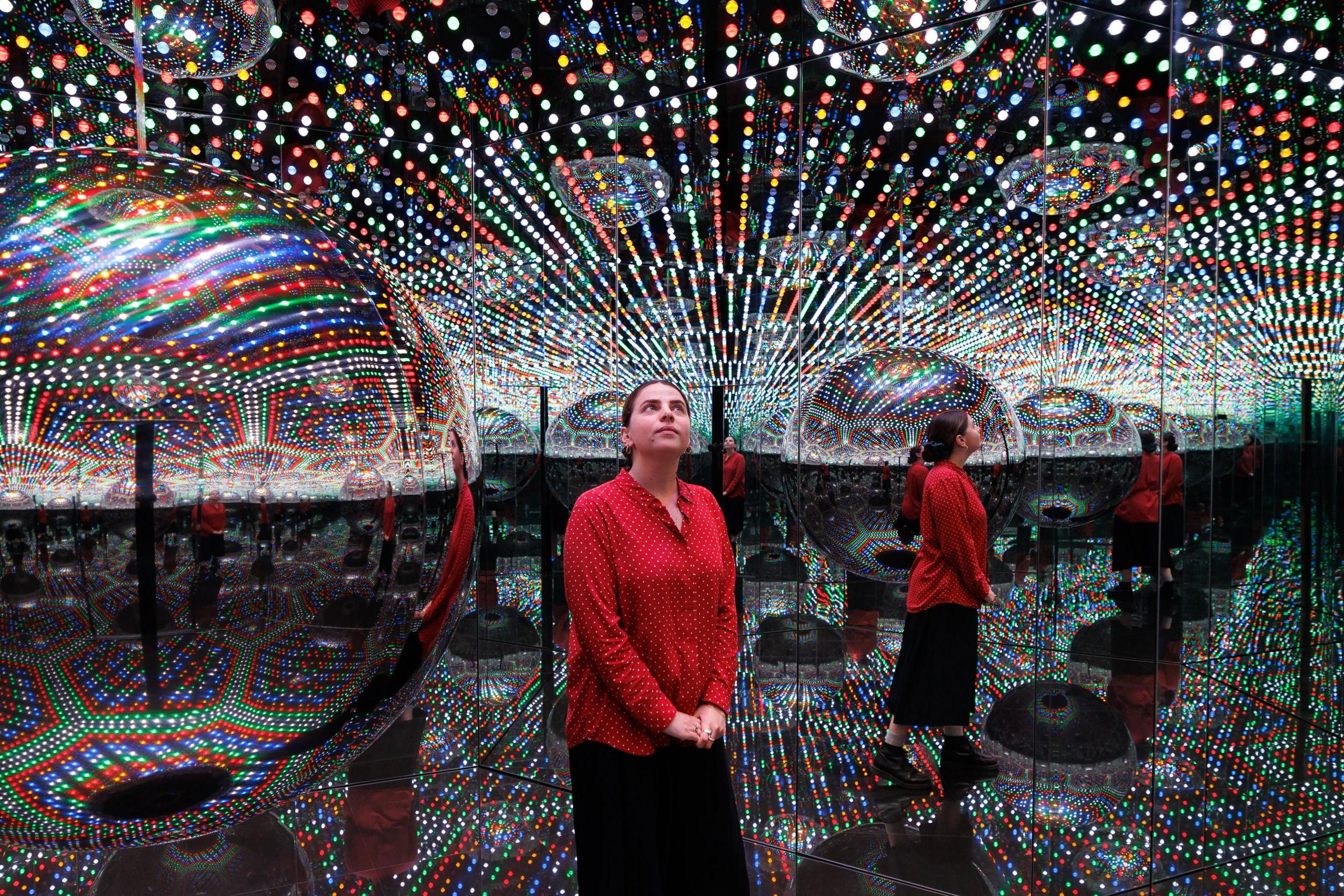 A visitor standing in one of Kusama's Infinity Rooms, seen reflected several times in mirrors surrounded by lights