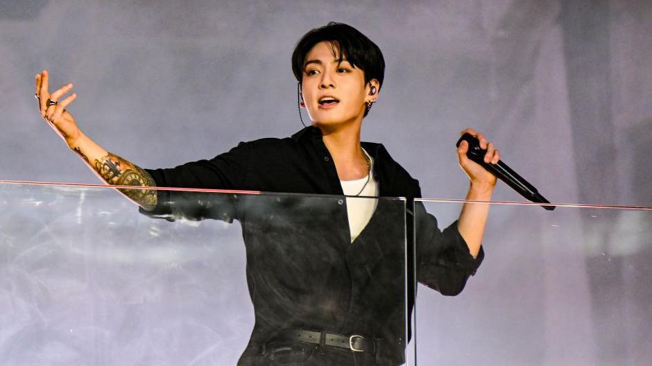 BTS vocalist Jungkook, in a black long-sleeved shirt, midway through a performance on stage
