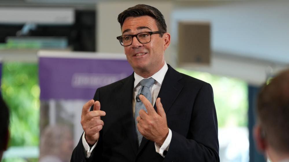 Prime Minister dressed in black suit with a tie talks to a crowd of people