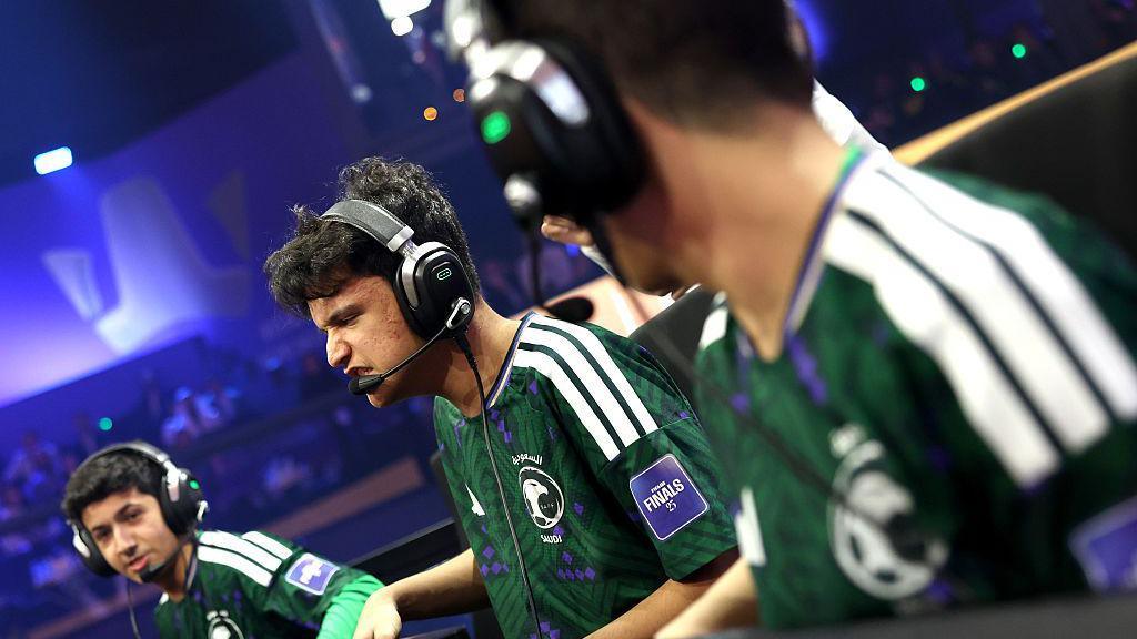 Three Esports players wearing green Saudi Arabia t-shirts in an arena, wearing black headphones with microphones on them