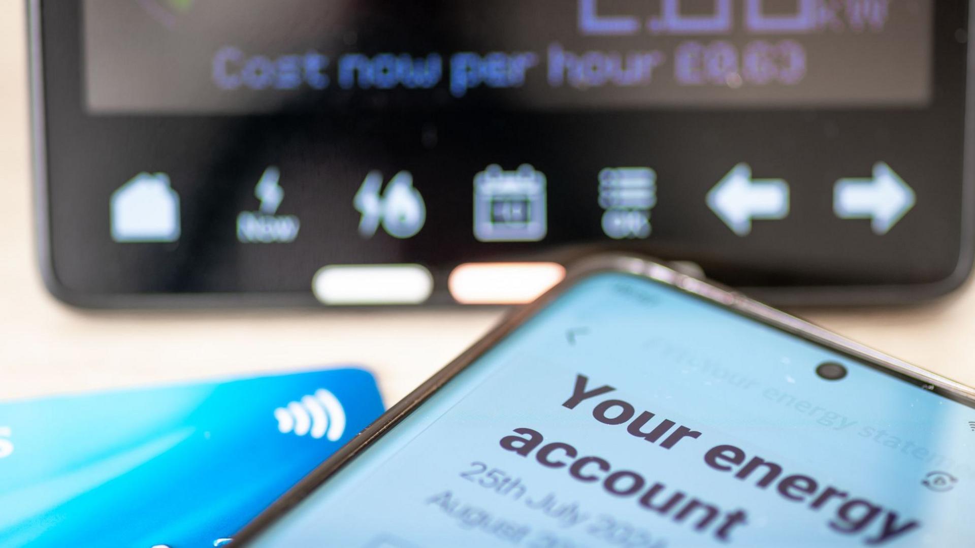 Smartphone displaying an energy account next to a bank card and in front of a smart meter display.