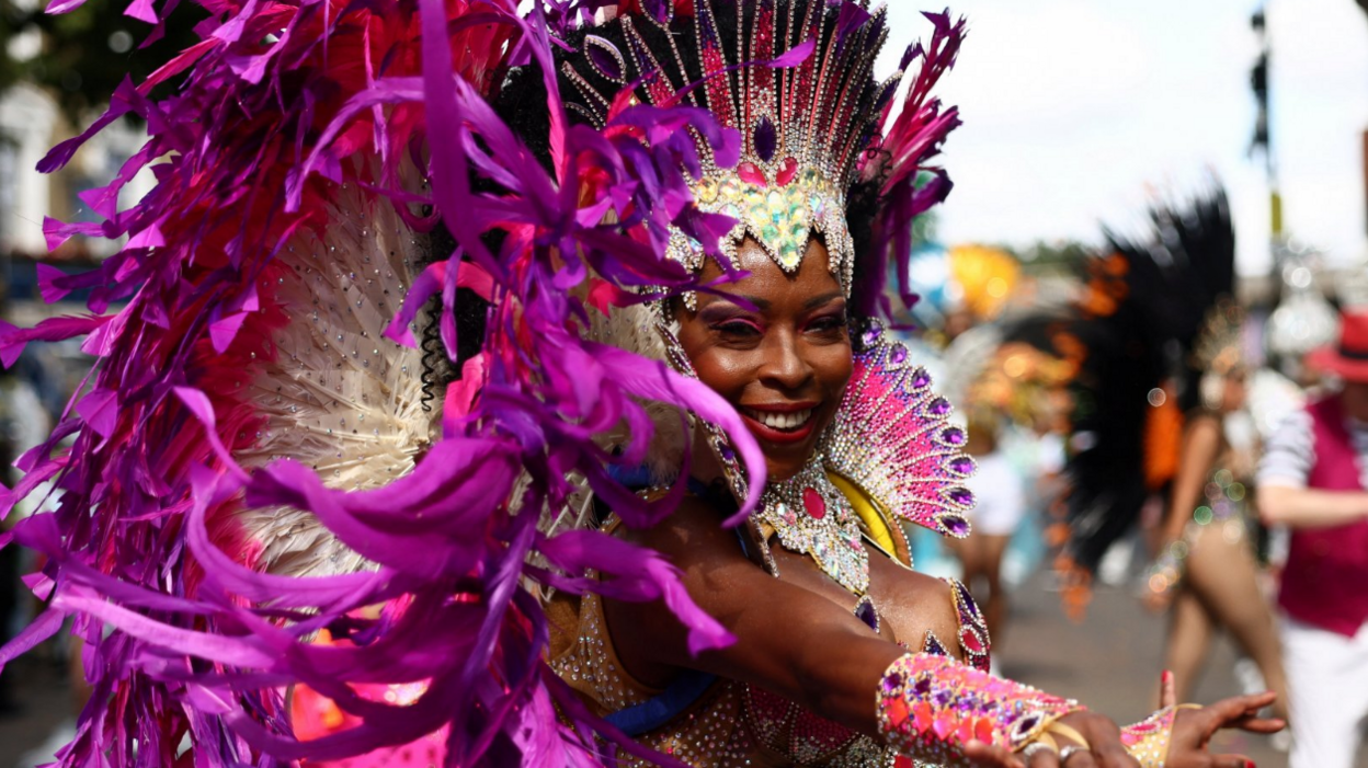 A woman in a purple and pink beaded costume and headdress with feathers smiles