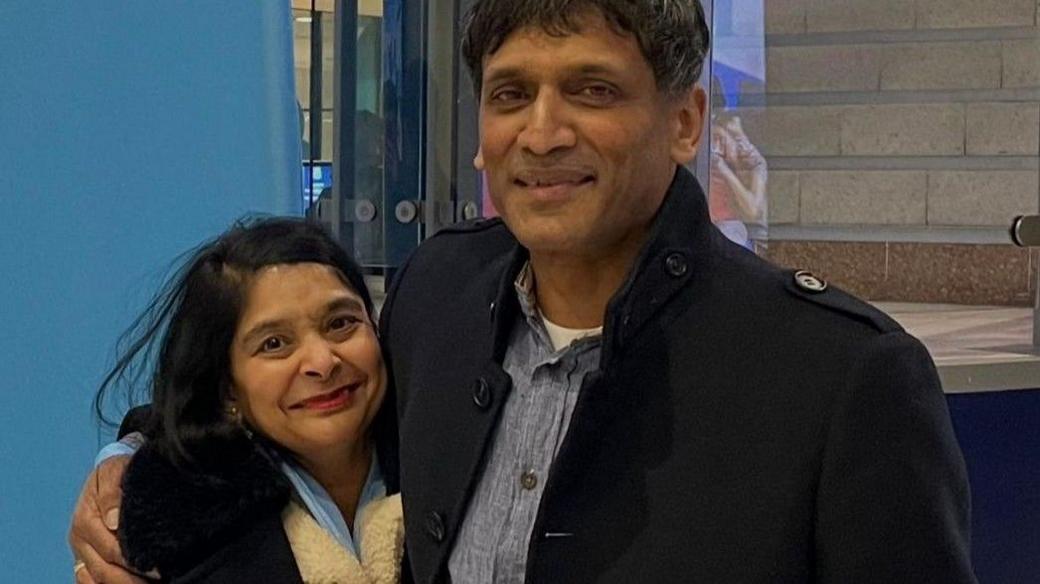 Bipin and Mala pose for a photo. Both wear coats and he has an arm around her shoulder