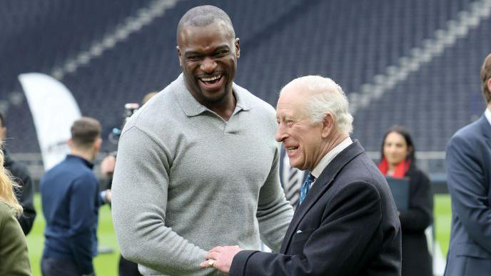 Efe Obada meets King Charles at an event to showcase the charitable work of Tottenham Hotspur and the NFL in February 2025