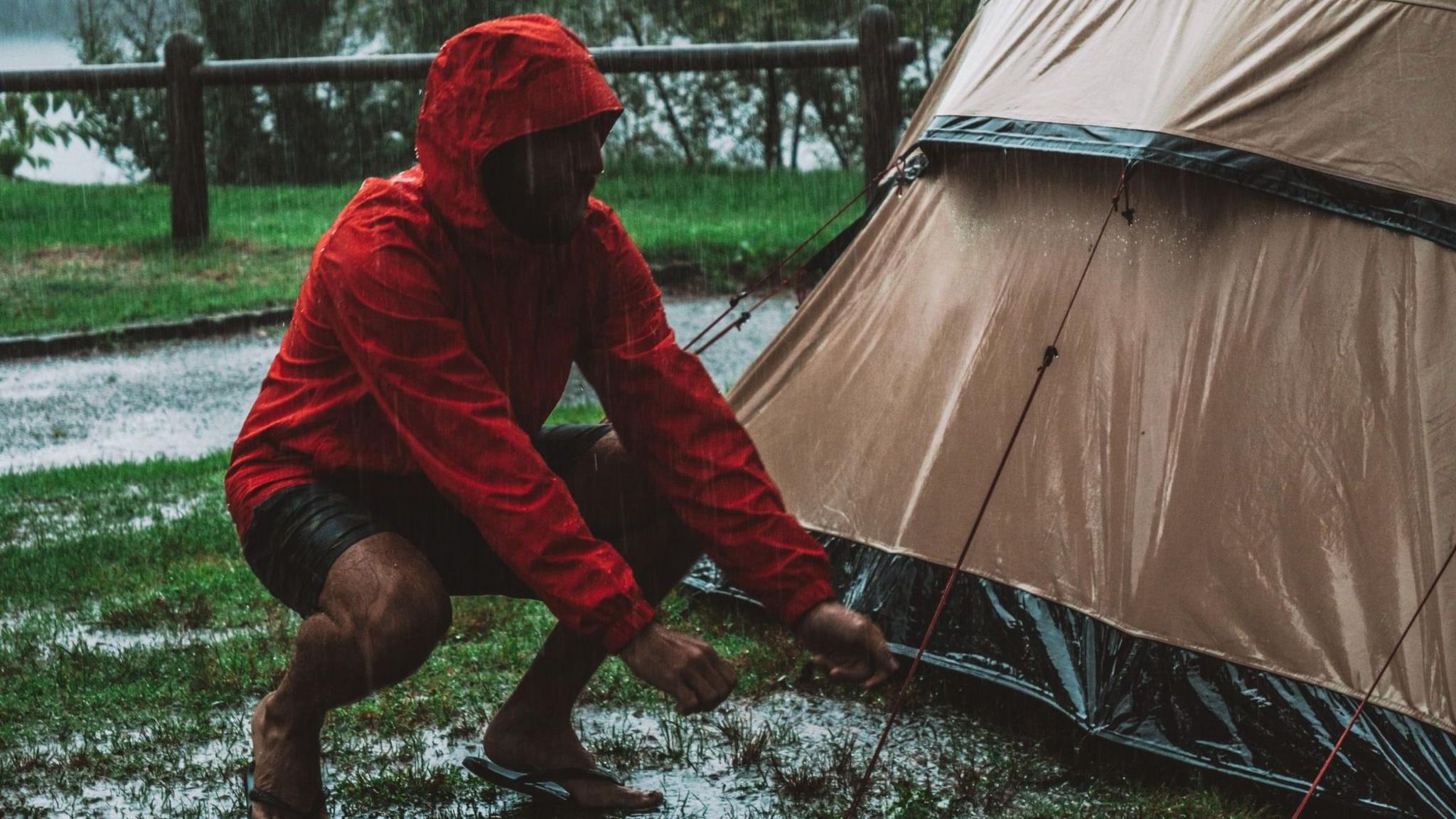 Man tethering down a tent in heavy rain