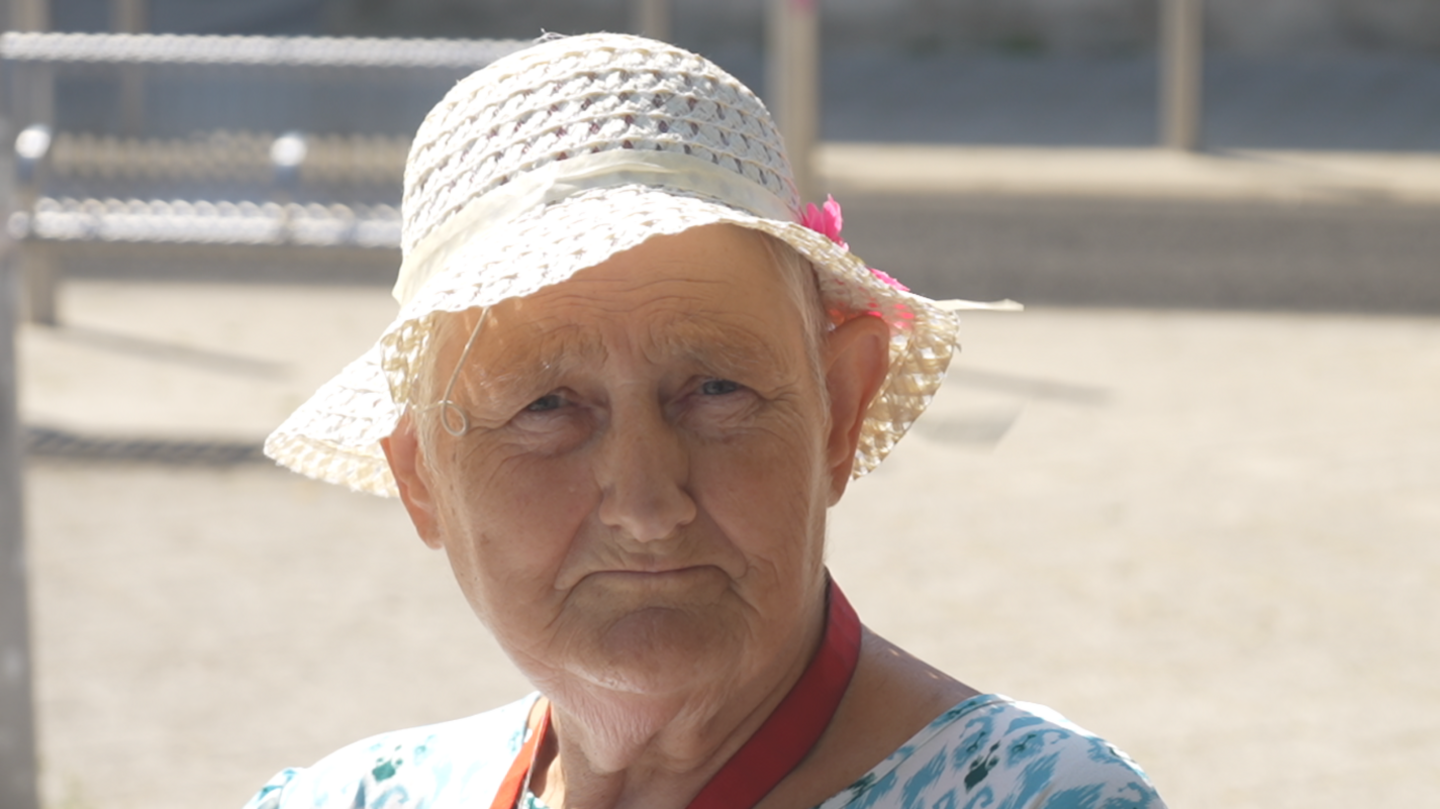Linda Robinson is wearing a cream hat and a white and blue dress in front of a large concrete area.
