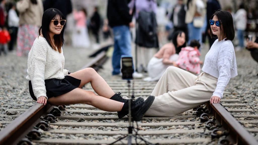 Two women pose for selfies as they visit the disused Gyeonghwa Station railway track during the Jinhae Cherry Blossom Festival in Changwon