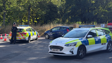 A police cordon with two police cars and a police officer.