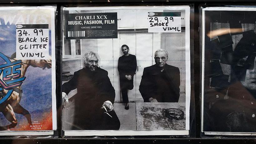 Charli XCX's Music, Fashion, Film vinyl cover in the middle of two other vinyl records. It's a black and white photo of John Cale, Marc Jacobs and Martin Scorcese.
