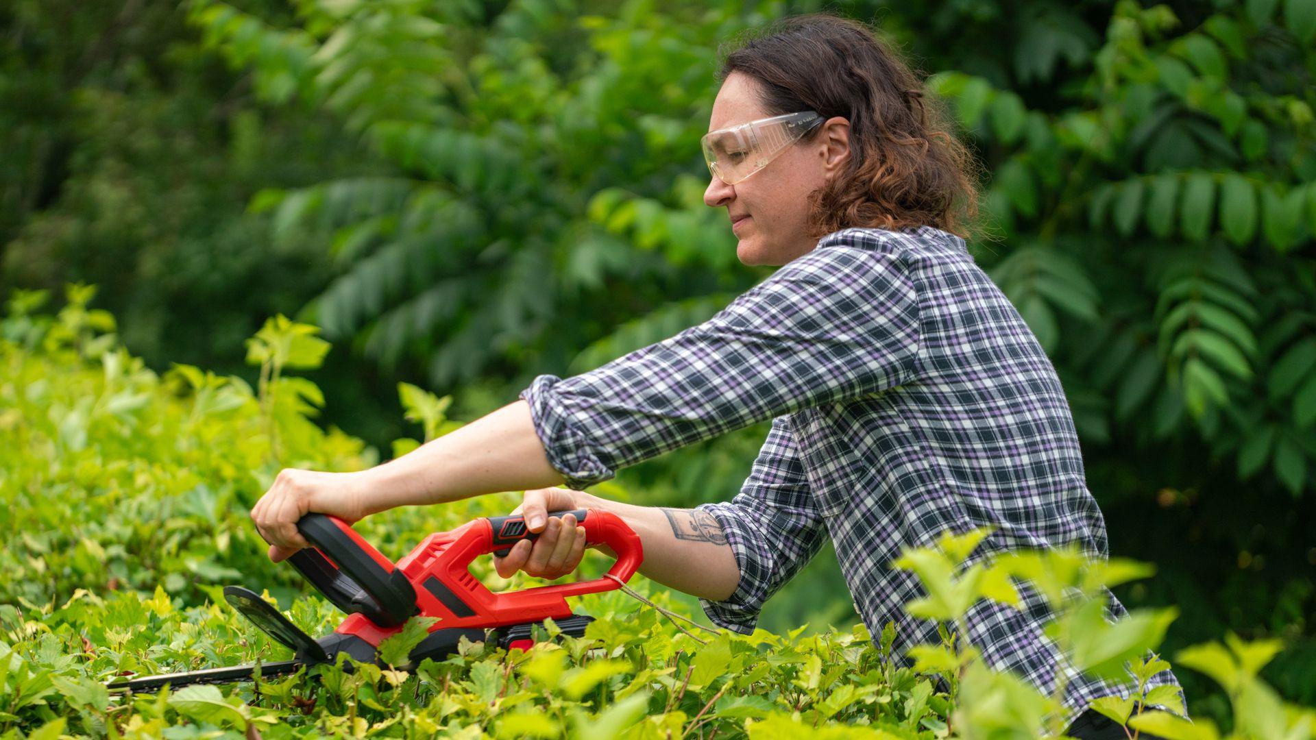 A woman trims a hedge whilst wearing goggles