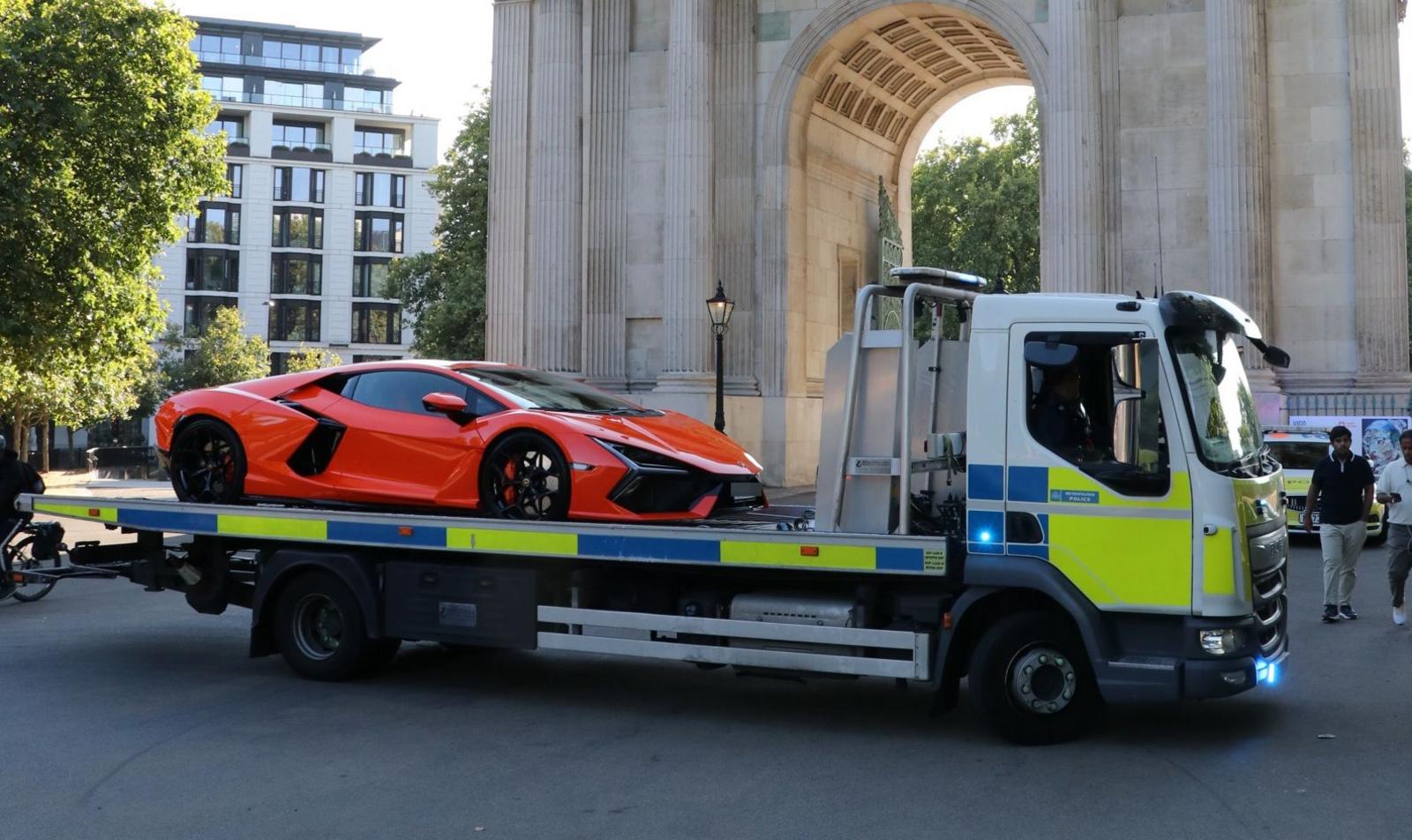 An orange Lamborghini supercar on a Metropolitan Police flatbed recovery truck beside Wellington Arch