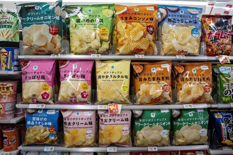 Shelves in a supermarket show packets of crisps in different colours