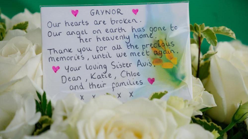 A message written on a card attached to a floral tribute reads: “Gaynor. Our hearts are broken. Our angel on earth has gone to her heavenly home. Thank you for all the precious memories. Until we meet again. Your loving sister Avis, Dean, Katie, Chloe and their families’ with what appears to be five kisses added below.