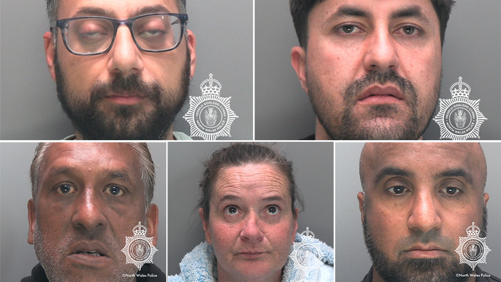A composite image of five police mugshots. Top right is a man with a dark beard and glasses. Top left is a man with a stubbly beard and moustache. Bottom left is a man with grey stubble. Middle bottom is a woman with scrapped back dark hair, and bottom right is a bald man with a black beard. They are all head shots and they are all looking at the camera.