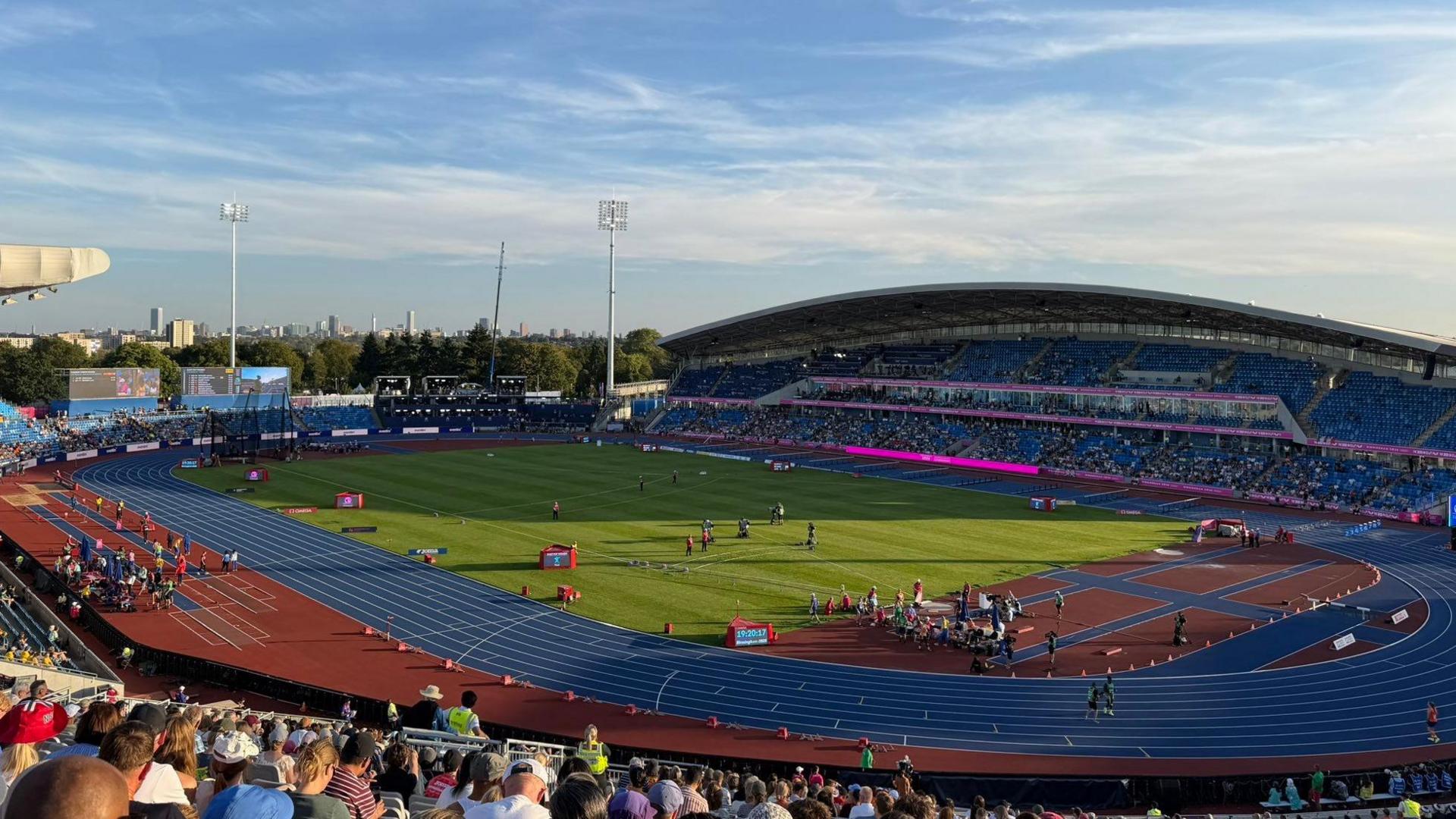 A photo of a stadium which is blue and orange with some pink. The grass in the middle is green.