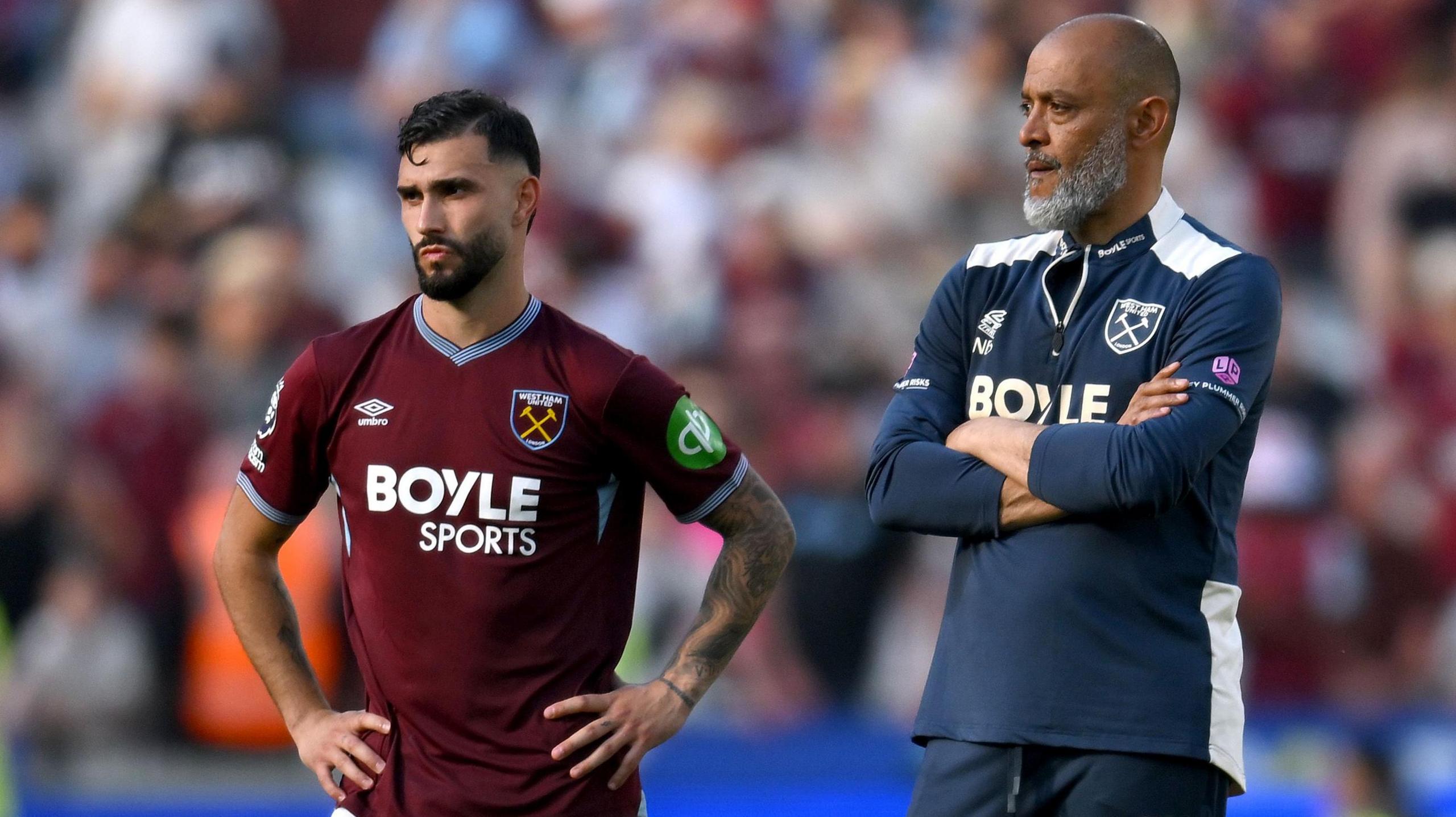 Taty Castellanos, wearing West Ham's 2025-26 claret home shirt with a light blue collar, stands with his hands on his hips looking dejected after relegation to the Championship on 24 May 2026. Nuno Espirito Santo, wearing a blue West Ham training top with white details, stands next to him with his arms folded