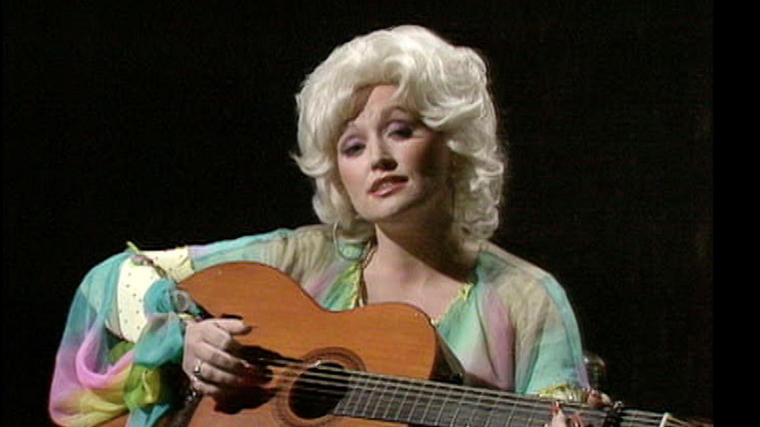 A young Dolly Parton playing an acoustic guitar