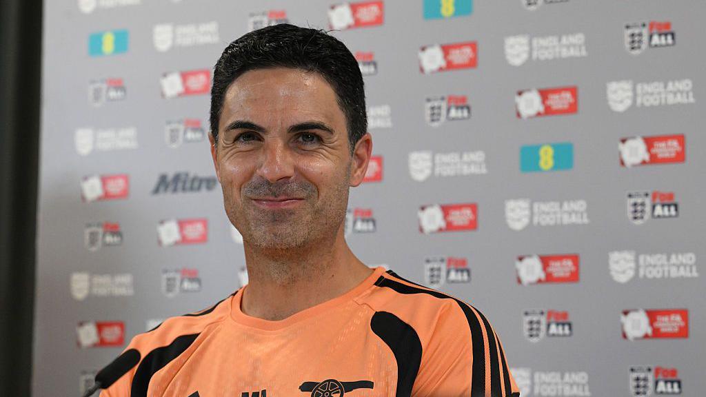 Mikel Arteta stifles a laugh while sitting at a press conference