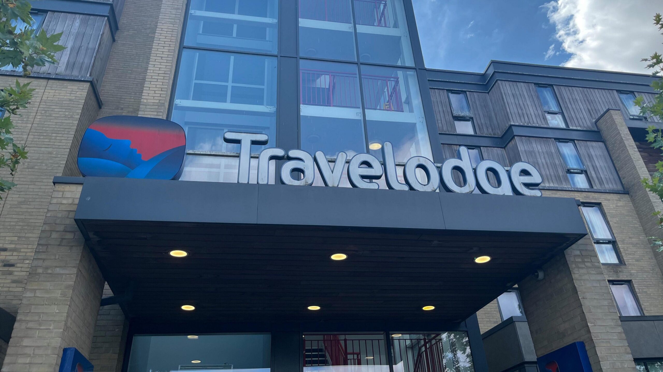 A Travelodge hotel on Newmarket Road in Cambridge. There is a Travelodge sign and logo on the entrance of the building.