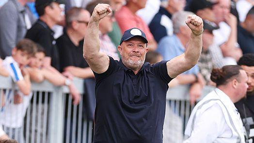 Andy Woodman, in a dark blue baseball cap and polo shirt, raises both arms to celebrate winning promotion with Bromley