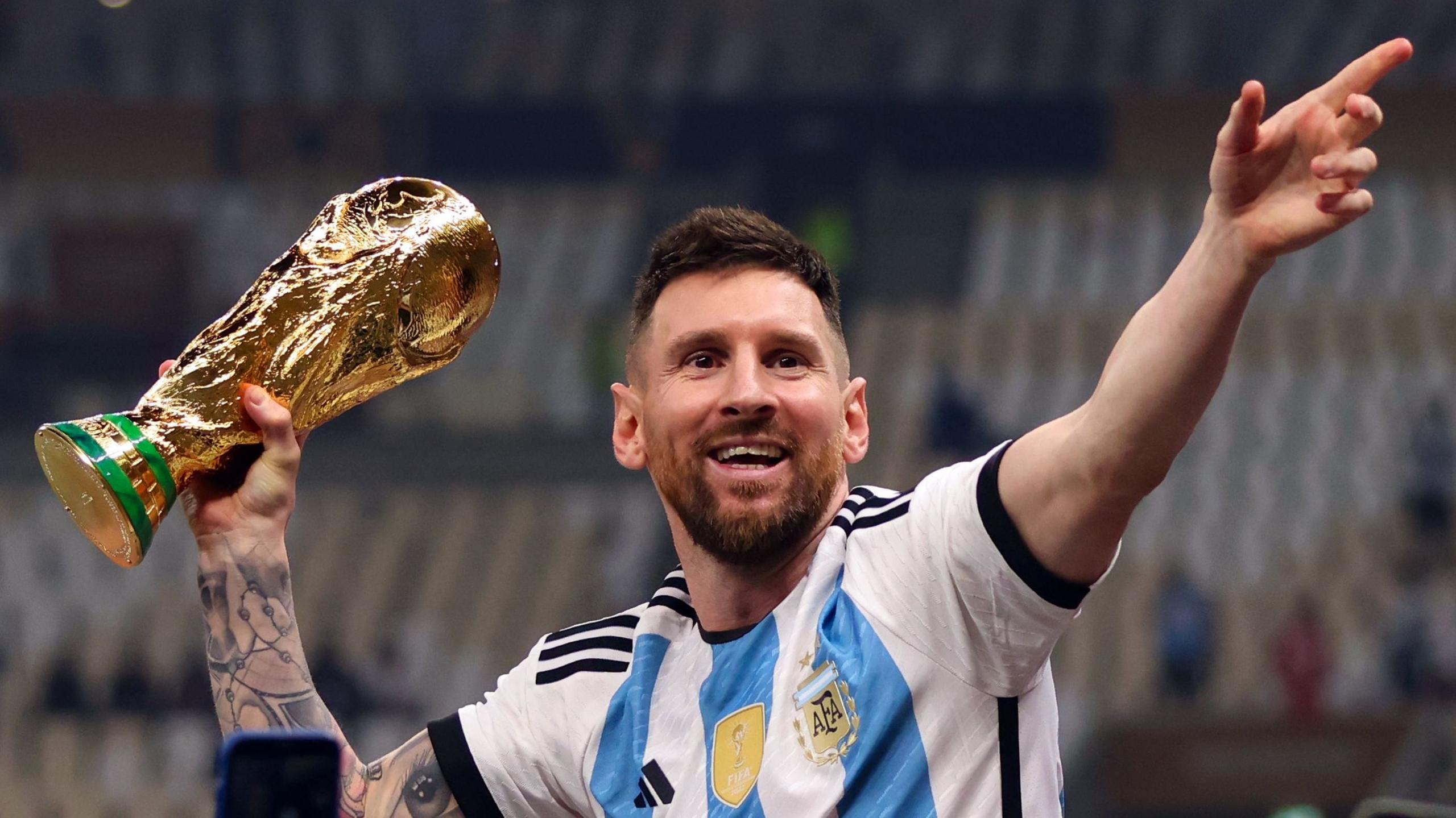 A jubilant Lionel Messi holds the World Cup trophy in his right hand after the 2022 final, won by Argentina