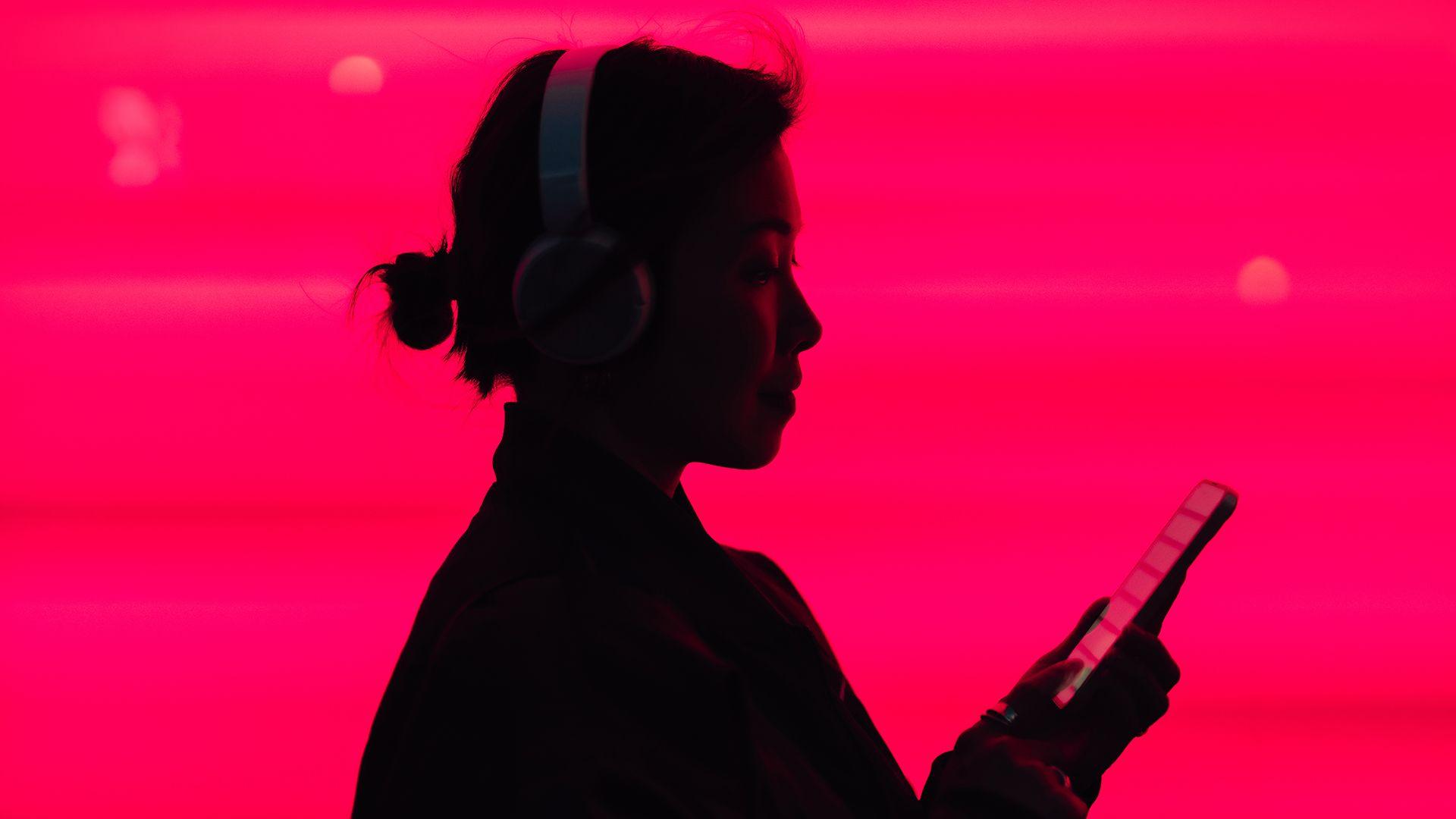 Woman in silhouette listening to music on smarphone in front of a bright pink background