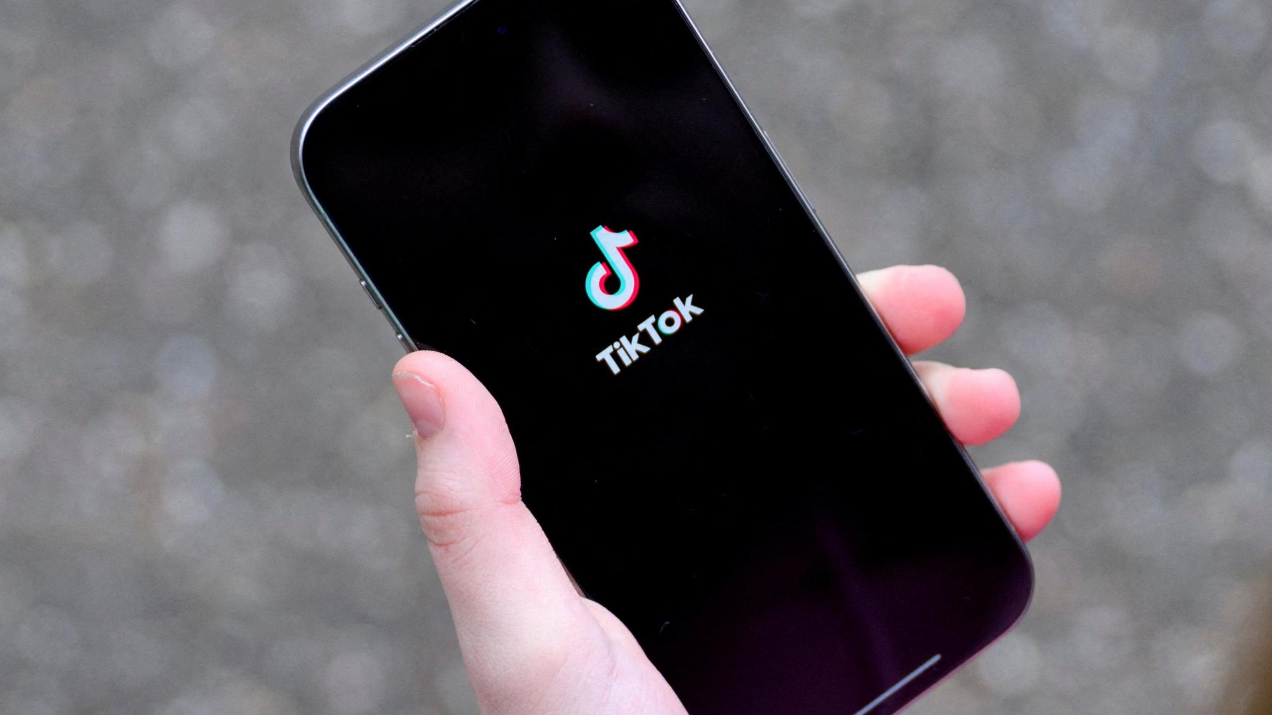 A young woman holding her iPhone while showing the TikTok app.