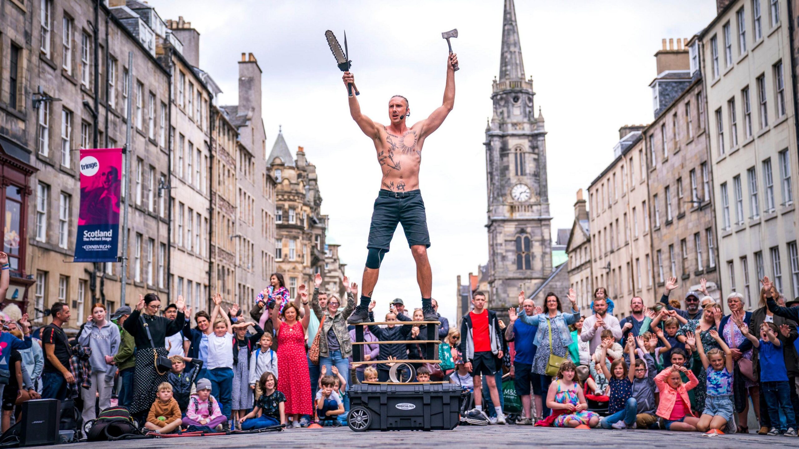 A bare-chested male street performer in front of a crowd on Edinburgh's Royal Mile.