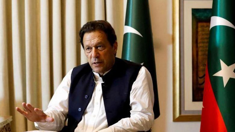 Former Pakistani Prime Minister Imran Khan speaks with Reuters during an interview, in Lahore, Pakistan March 17, 2023. He can be seen seated with his hand outstretched and speaking. Two Pakistani flags are behind him.