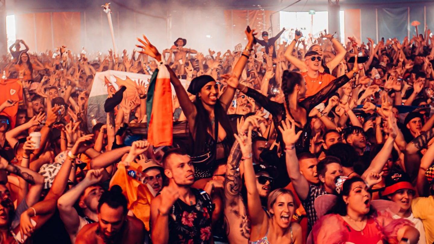 A large crowd of people at Creamfields are facing a stage with their arms in the air.