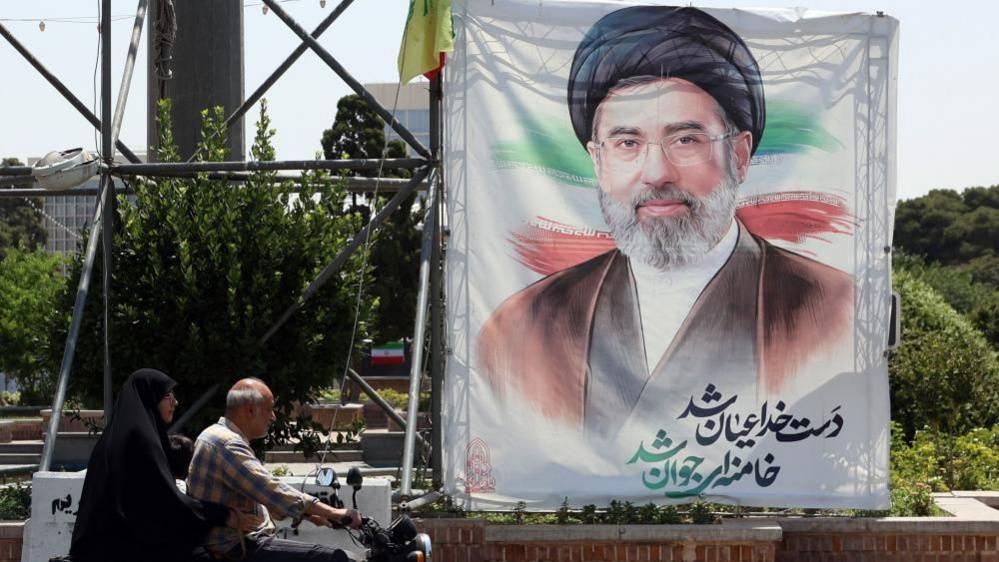 People drive next to a billboard of Iranian supreme leader Ayatollah Mojtaba Khamenei