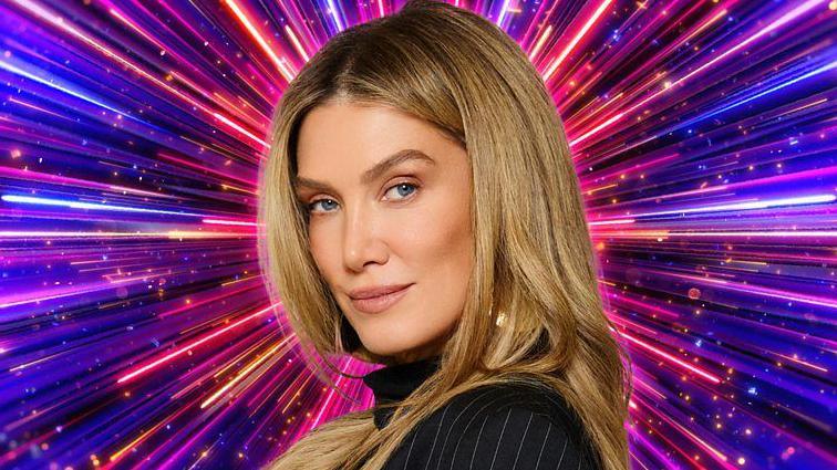Delta Goodrem in front of a graphic showing numerous purple, pink and blue lines radiating from the centre, in a Strictly promotional photo