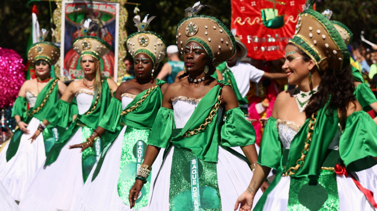 A group of five women in matching white and green dresses perform in the parade.