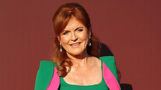 Sarah Ferguson, with her dark red hair half tied up, in a green dress and fuchsia dress and diamond earrings
