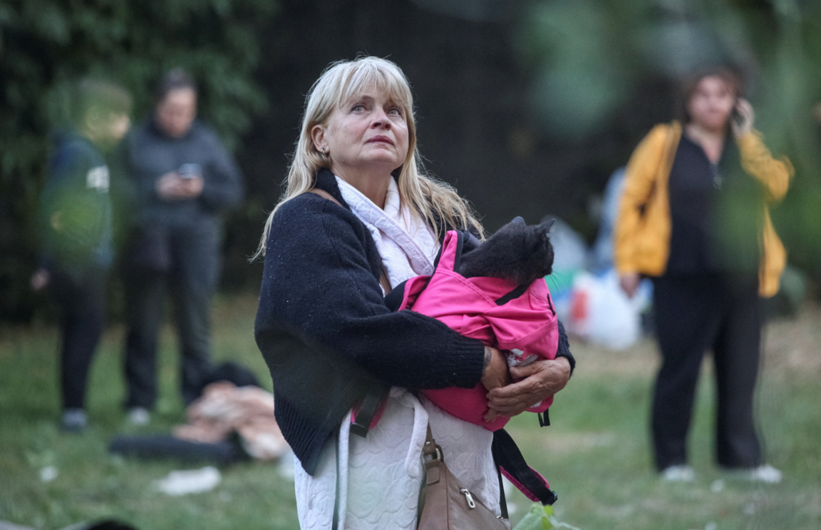 Larysa standing holding her black cat in a pink bag looking up as people in the background stand around