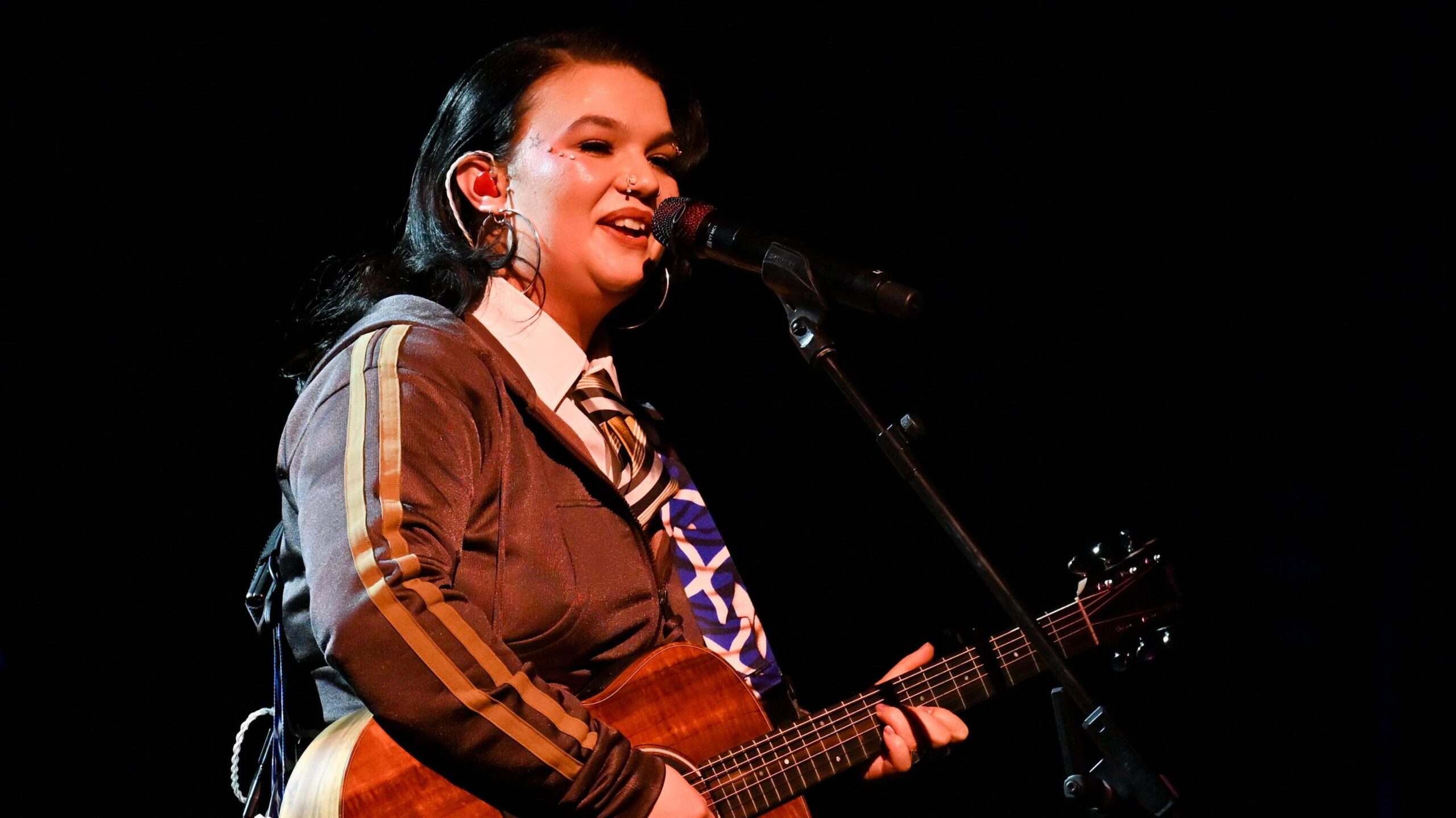 Lola young on stage playing an acoustic guitar and singing into a microphone