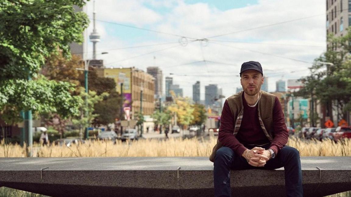 Matteo Sgaramella sits on a concrete slab with the skyline of Toronto in the background
