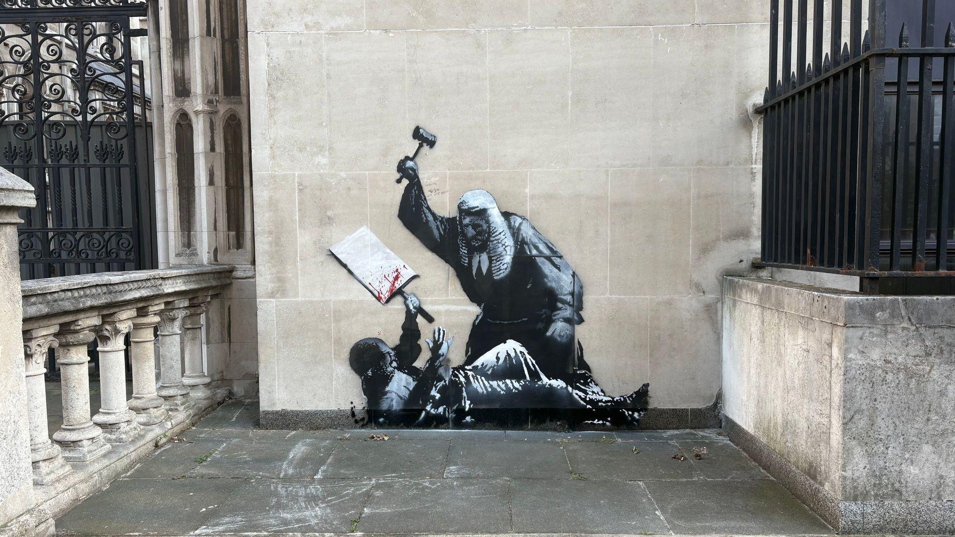 A stencilled mural on a wall of the Royal Courts of Justice in London, depicting a judge in a wig battering a protester with his gavel. The protester is lying on the ground holding a placard with blood on it.