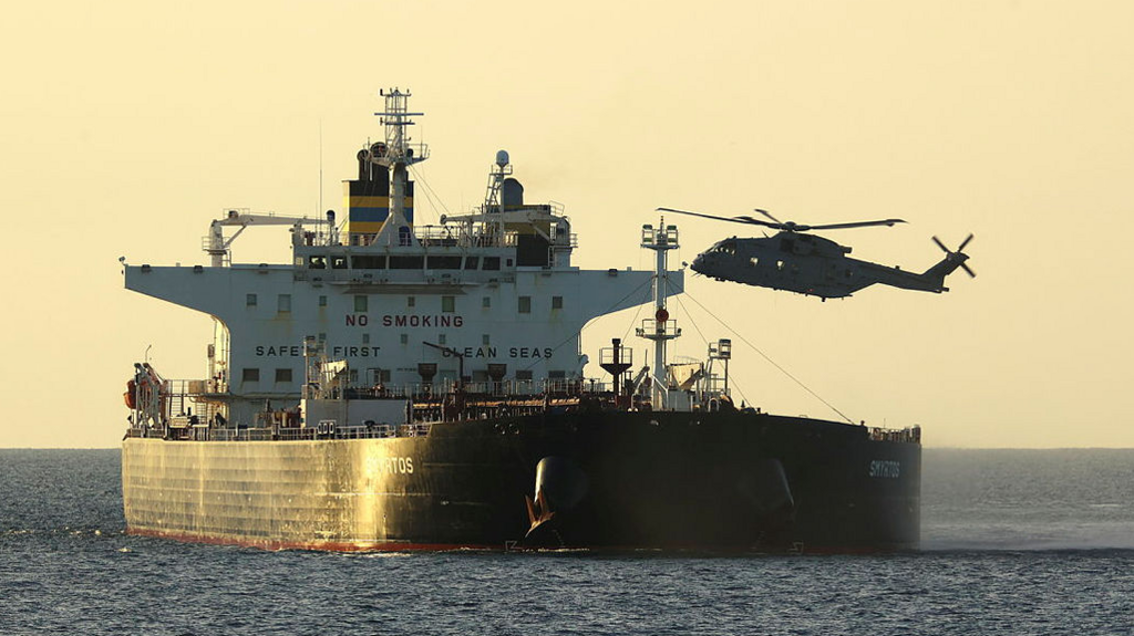 A large black and white boat on the sea with the word 'Smyrtos' on the side. A helicopter hovers just above it.