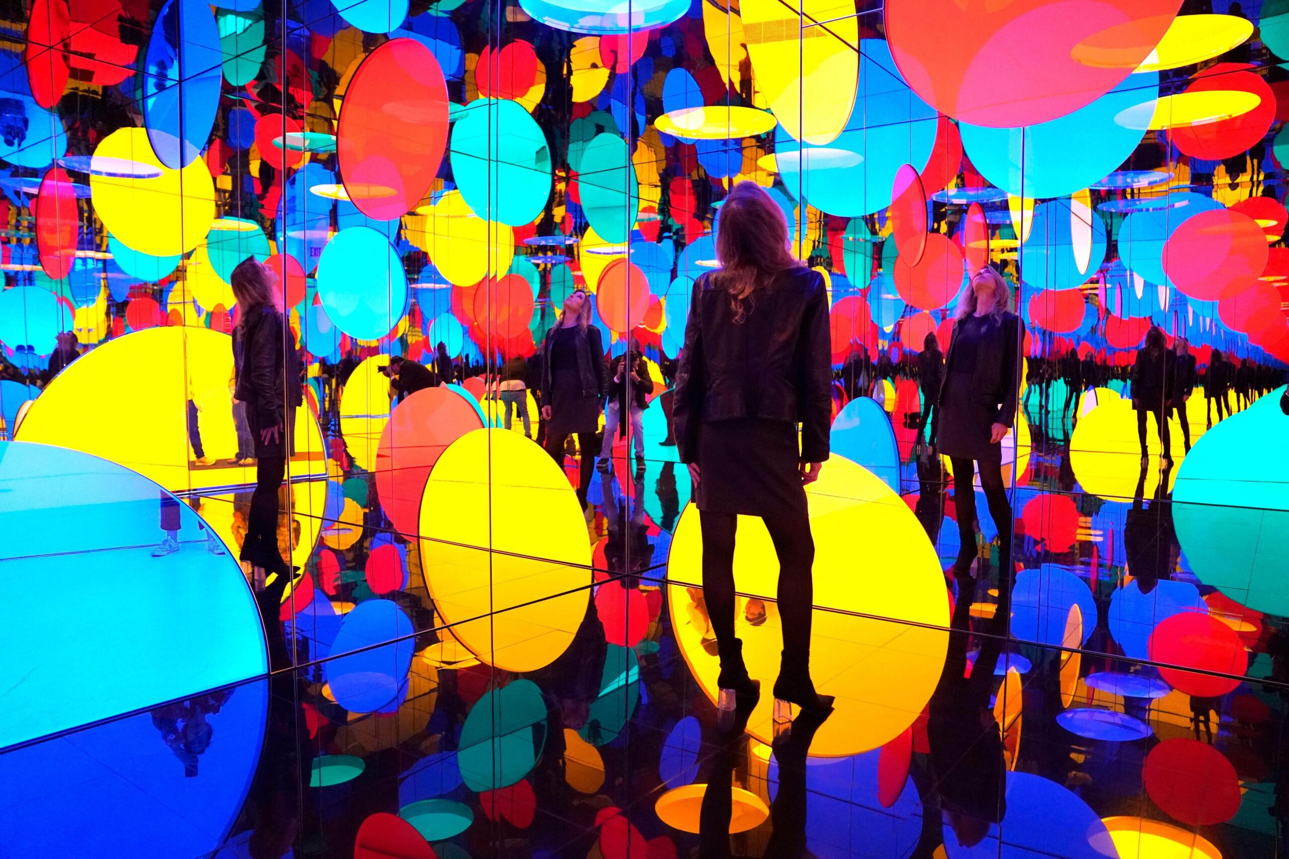 A gallery visitor standing in a mirrored room containing lots of brightly coloured circles and their reflections