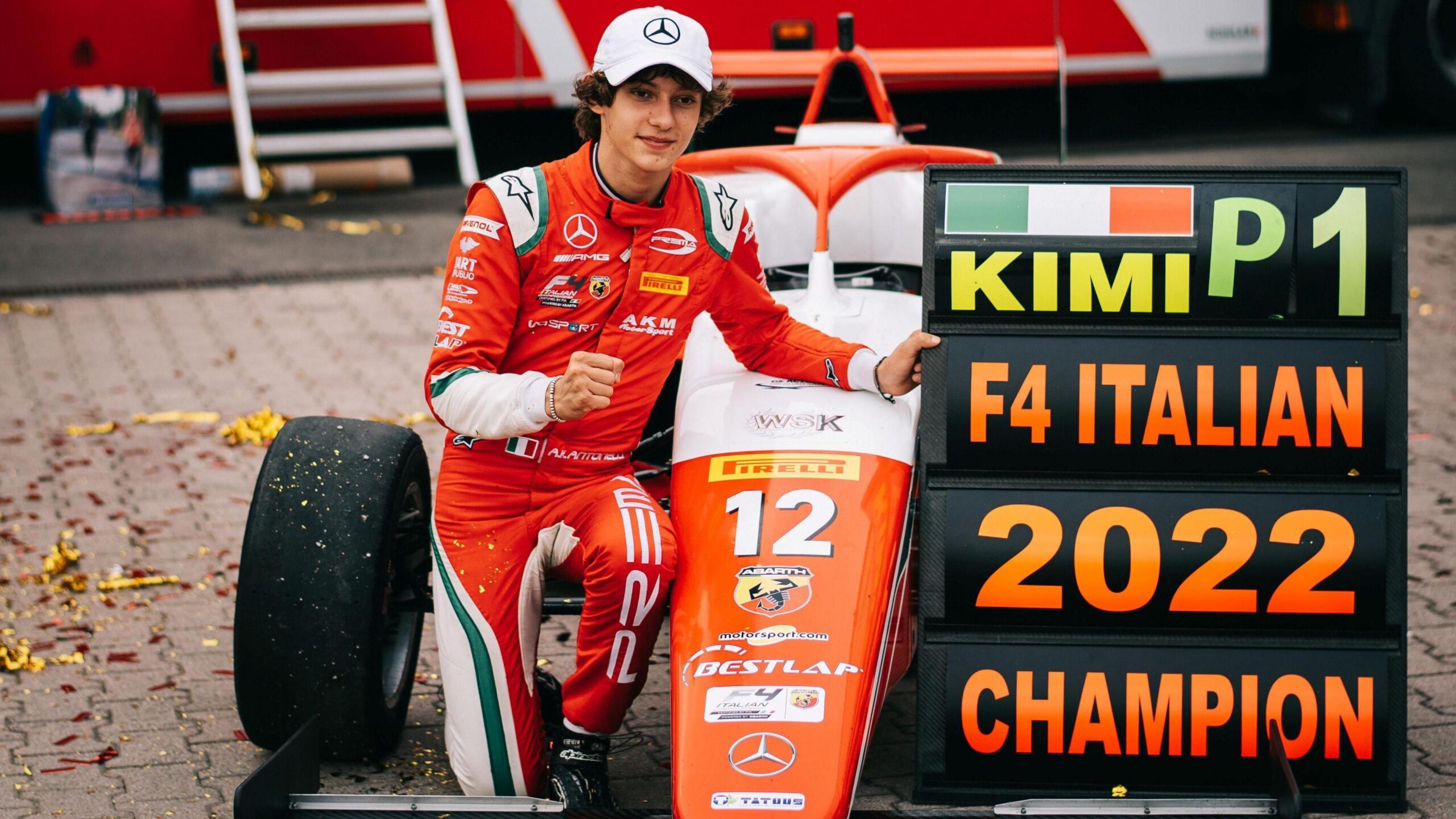 Kimi Antonelli poses for a picture alongside his racing car and a pit board side that refers to him winning the 2022 Formula 4 championship