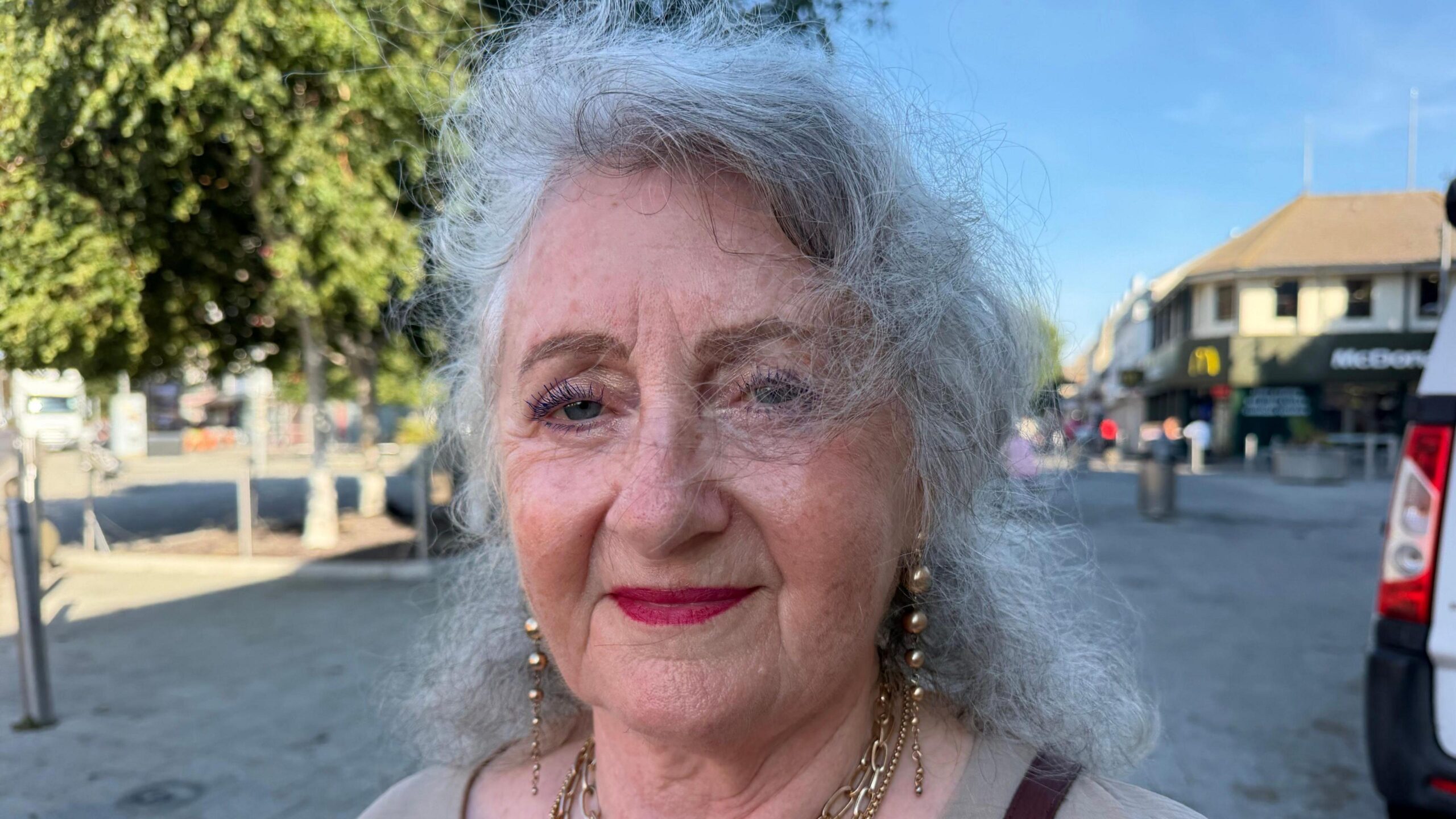 Jenny Hopkins has shoulder-length grey hair. She is wearing golden jewellery and smiling in Clacton town centre.
