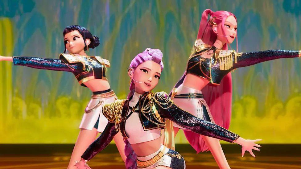 Picture of the animated band HUNTR/X, which is made up of performers Ejae, Audrey Nuna and Rei Ami who appear as cartoon characters in matching bolero jackets, A-Line skirts and an assortment of colourful wigs in pink and purple.