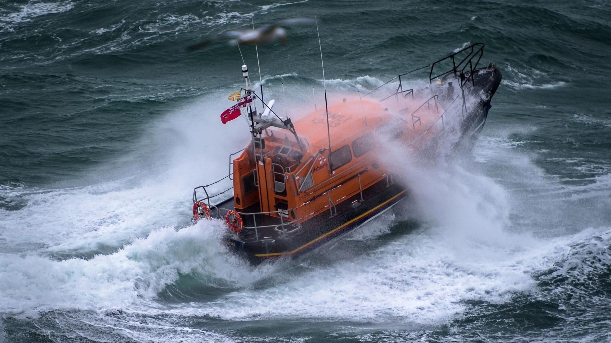 A Shannon class lifeboat in rough swell with a wave breaking over it.