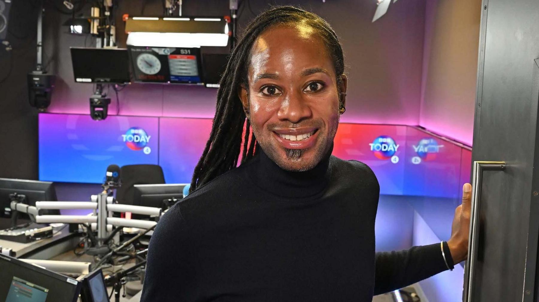 Dressed in a black turtle neck and trousers, Jason Arday smiles at the camera in a BBC Radio 4 studio.
