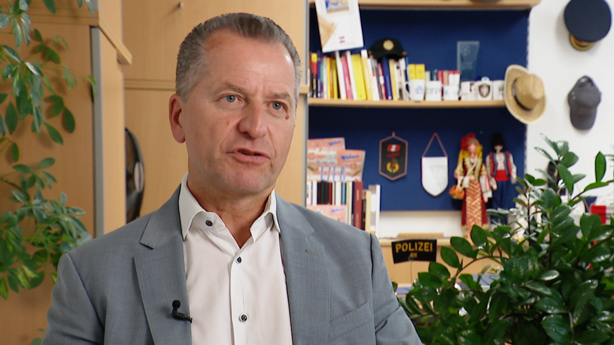 Gerald Tatzgern, a man with short, grey hair, wearing a light grey suit and a white shirt, sitting in an office with books, pot plants and police memorabilia behind him.