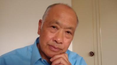 Tom Darwood, Joseph 77, looks at the camera with his left hand's finger bent under his chin. He is wearing a light blue collared shirt.