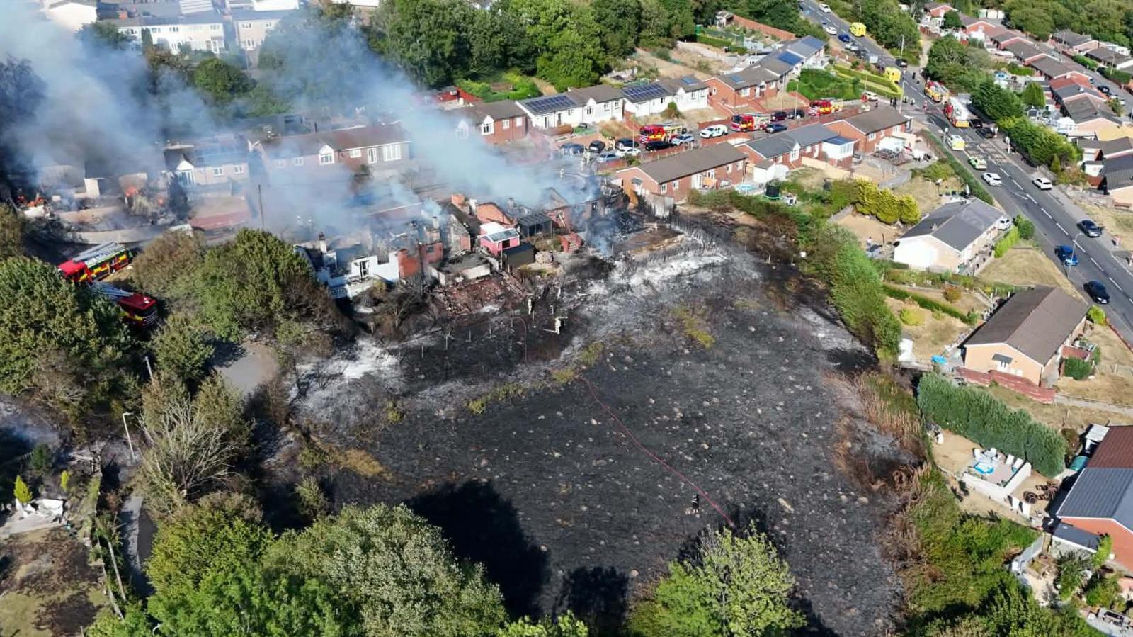 An aerial photo of the scene, showing the full extent of a blackened patch of land. The burned homes are on a resident street, with another row of housing behind.