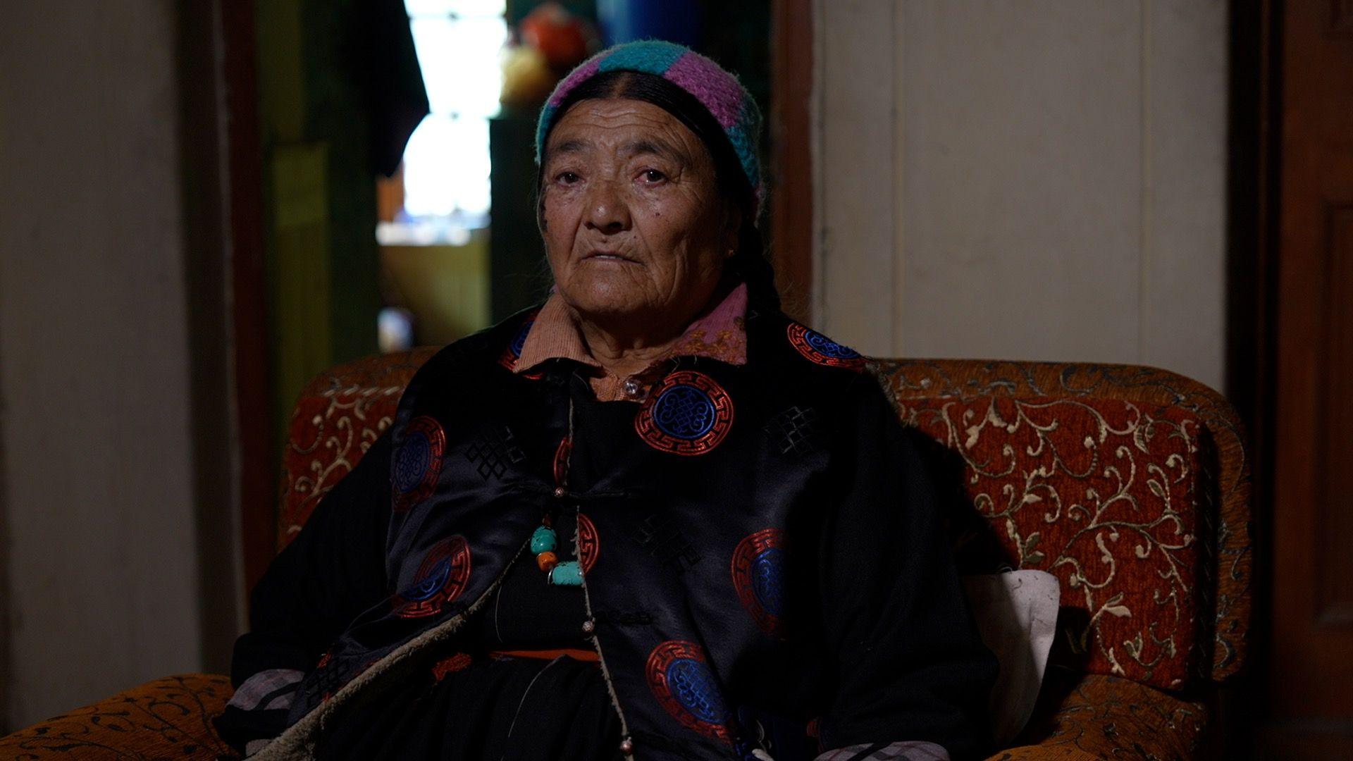 Morup's wife Yangskit dressed in a black Sulma, a traditional Ladakhi robe and a colourful knitted headcover with traditional jewellery around her neck symbolising Ladakh's heritage and Buddhist spirituality